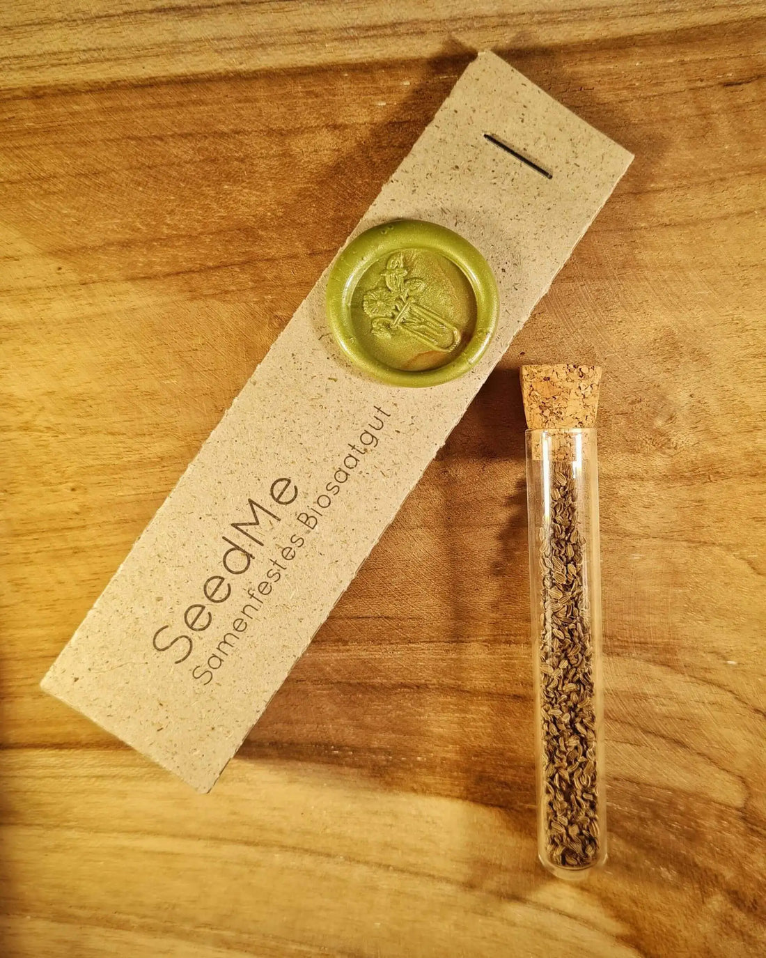 Samen für orangene Möhre im Reagenzglas, daneben eine Graspapierverpackung von SeedMe